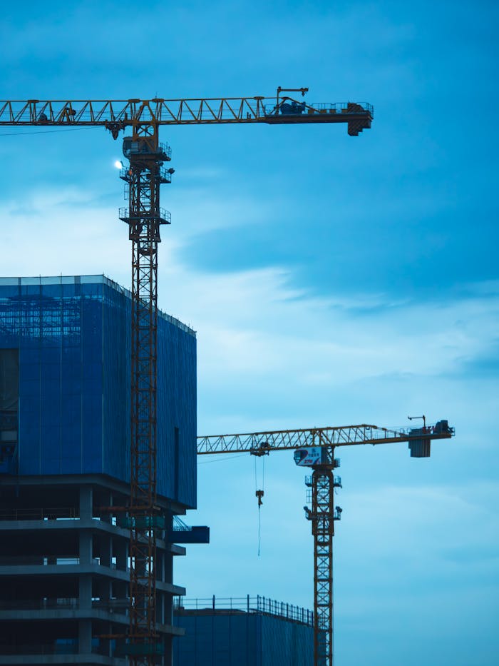 about-img Tall cranes at a construction site against a twilight sky in the city, capturing urban development.